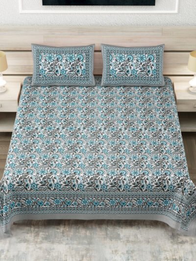 A double bed made with a Jaipuri pure cotton bedsheet in shades of turquoise and black with traditional mandala designs, flanked by two wooden nightstands with beige lamps.