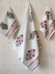 Three red and white hand-embroidered towels, including a hand towel and a bath towel, elegantly displayed on a wall.