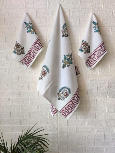 A set of three towels, including hand and bath towels, elegantly displayed on a wall alongside a potted plant.