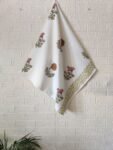 A hand towel placed on a white tablecloth featuring an elegant white and green floral pattern.