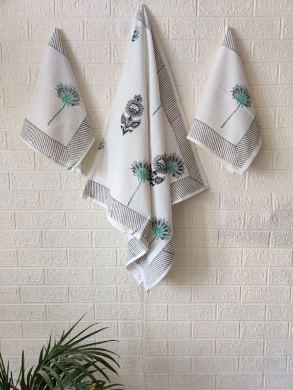 . A set of three towels, including one bath towel and two hand towels, featuring white fabric with delicate blue and green flower designs.