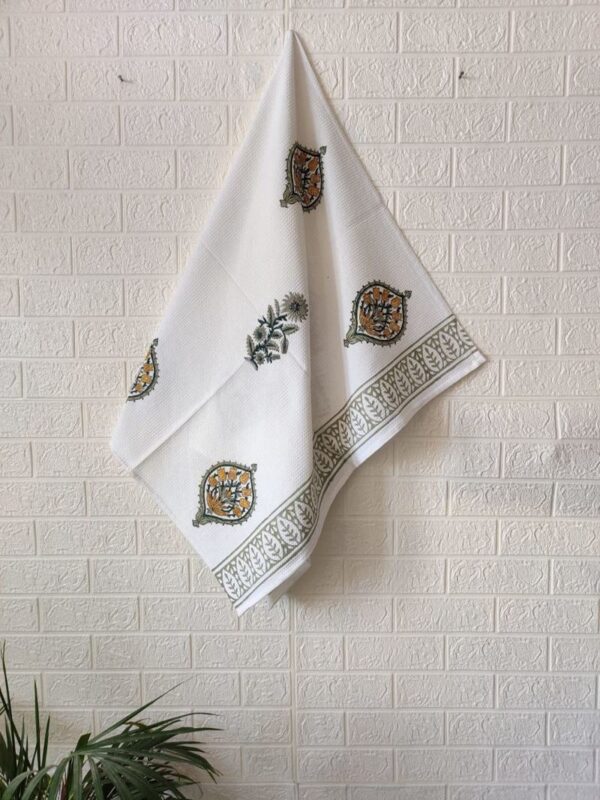 A set of three white towels adorned with green and yellow patterns, consisting of a hand towel and a bath towel.
