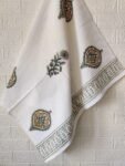 A set of three white towels adorned with green and yellow patterns, consisting of a hand towel and a bath towel.
