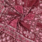 A curled up single bedsheet showcasing a vibrant paisley print in shades of red and pink, with a large paisley design as the focal point