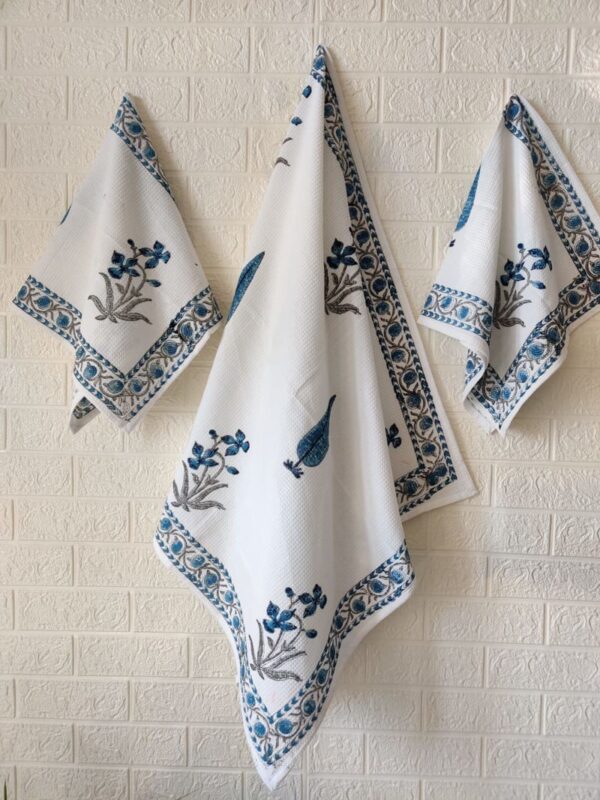 Three blue and white towels, including a bath towel and hand towel, neatly hung on a wall.