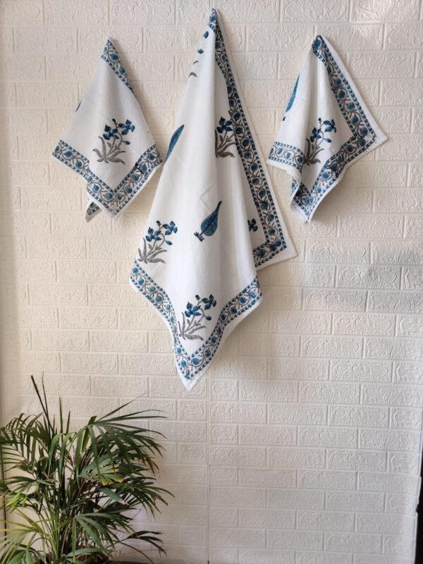 Three blue and white towels, including a bath towel and hand towel, neatly hung on a wall.
