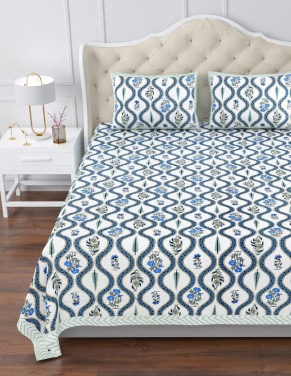 Close-up of a king size bed with a blue and white bedspread featuring a jaal print and flowers.