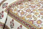 A close-up of a floral bedspread. The design includes maroon, yellow, and pink flowers with green leaves, accented by an ornate border with circular floral motifs along the edge.