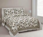 A green and white paisley print double dohar made from mulmul cotton, displayed on a bed in a bedroom setting