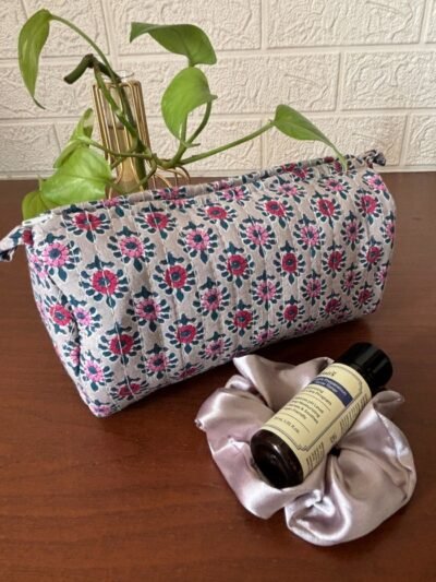 A medium, round toiletry bag crafted from colorful fabric scraps in a patchwork design. It features a gold zipper closure for secure storage and a wrist strap for easy carrying.