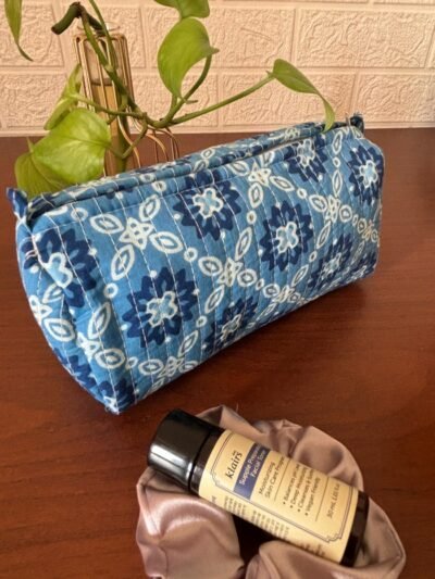 A colorful, handcrafted toiletry bag with a floral patchwork design made from cotton fabric. It has a zipper closure and a wrist strap. The bag is sitting on a wooden table.
